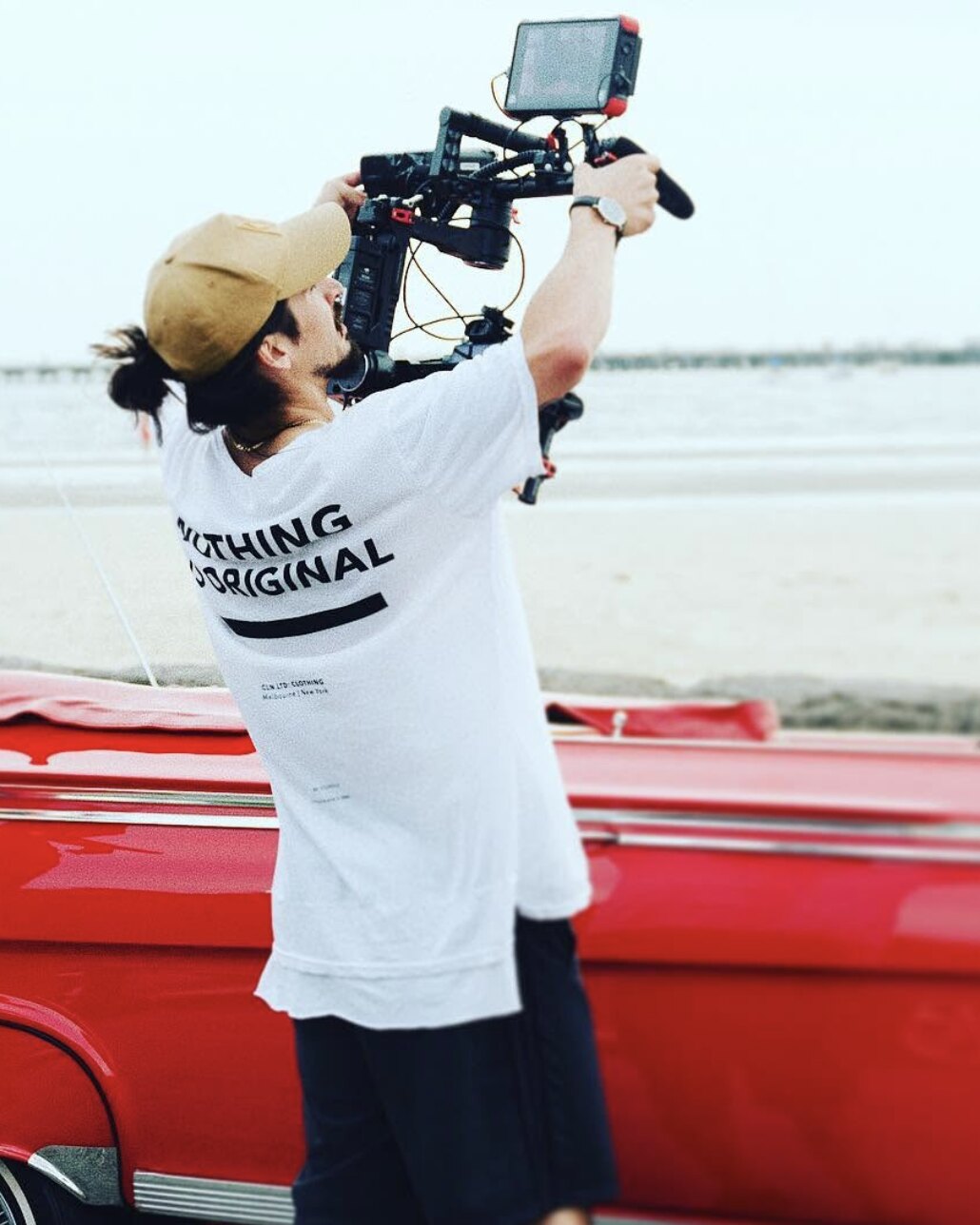 Tim McCartney filming over a red classic car at the beach