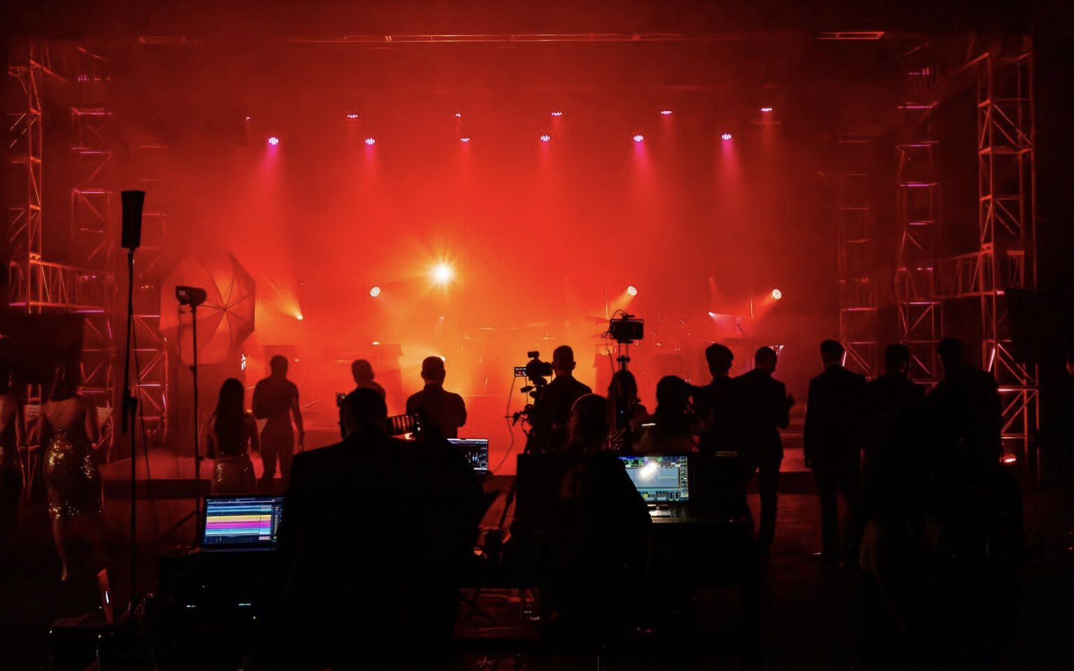 Crew and monitors in front of a lit stage during a live production